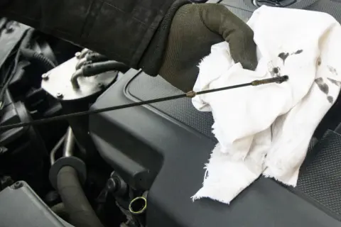 Sprawdzanie poziomu oleju w silniku fiat stilo 1.9 jtd. Ręka w rękawiczce wyciera bagnet.