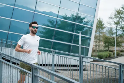 Uomo con occhiali da sole corre su una rampa metallica, godendosi i suoi 30 secondi di recupero tra le serie di allenamento.
