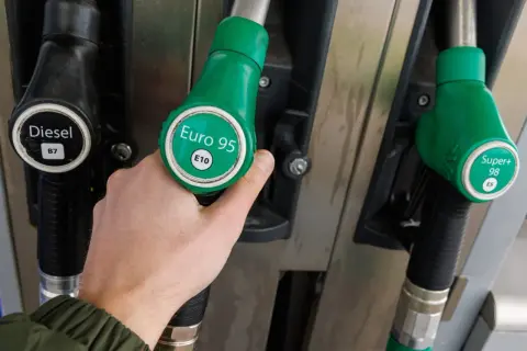 Dłoń wybiera dystrybutor z napisem Euro 95 E10. Obok widać Diesel B7 i Super+ 98 E5.