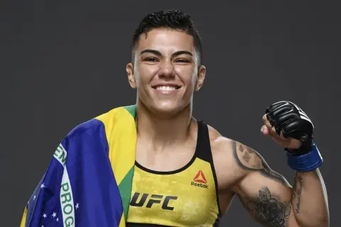 Jessica Andrade, MMA-fighter, ler glatt med Brasiliens flagga över axeln och en boxningshandske på sin högra hand.