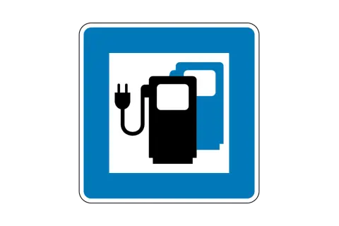 Blaues Schild mit weißem Rahmen. Darin zwei Zapfsäulen-Symbole, eins schwarz mit Stecker, eins blau. Bedeutung: Ladestation für Elektroautos.
