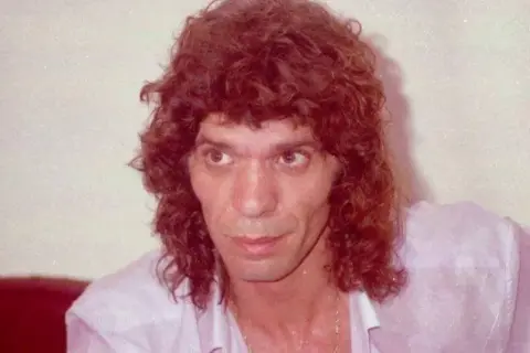 Primer plano de un hombre con cabello rizado y camisa rosa. Se especula a qué edad murió Camarón.