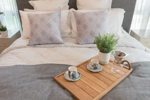 Eleganckie ścielenie łóżka z dwoma ozdobnymi poduszkami i tacą z kawą.
