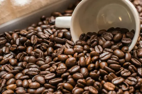 Chicchi di caffè tostati, con una tazzina bianca rovesciata in mezzo. Un'immagine che evoca il piacere del caffè senza caffeina.