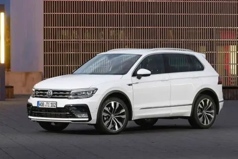 Biały Volkswagen Tiguan 2019 z eleganckimi felgami stoi przed nowoczesnym budynkiem z drewnianą fasadą.