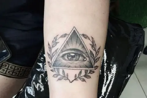 Oko proroka tatuaz w trójkącie otoczone gałązkami. Symbol czujności i wiedzy.