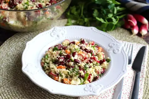 En härlig couscous sallad med bönor, rädisor och örter serveras på en vit tallrik.
