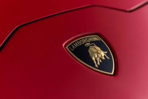 Złote logo Lamborghini z bykiem na czerwonym tle, symbol luksusowych marek samochodów.