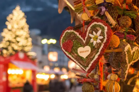 Corazón decorado con "Welcome" en un mercadillo navideño de Calatayud. Luces de árbol y puestos de feria al fondo.