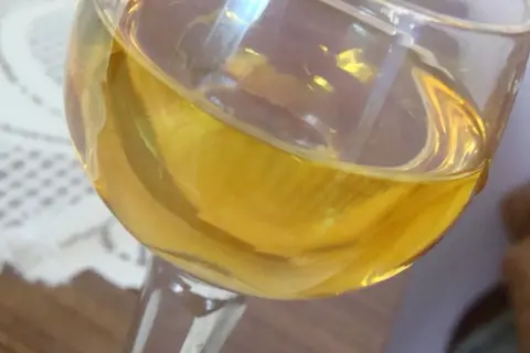Złocisty płyn w kieliszku, być może aromatyczne wino mandarynkowe, odbija światło.