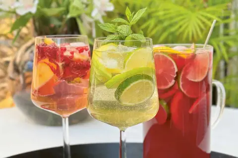 Tre glas med alkoholfri sangria fyllda med frukt och is. En kanna med röd sangria i bakgrunden.