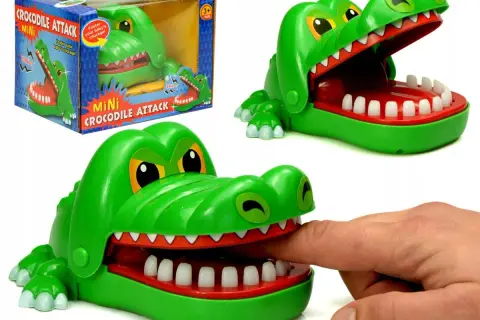 Zielona zabawka gra krokodyl z otwartą paszczą, do której włożono palec. Obok pudełko z napisem "Mini Crocodile Attack".