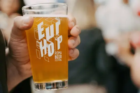 Un bicchiere di birra dorata con il logo "Eur Hop Roma Beer Festival" tenuto in mano.