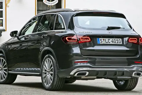 Ciemnoszary Mercedes-Benz GLC 300e z eleganckimi światłami LED i chromowanymi końcówkami wydechu, zaparkowany przed budynkiem z oknem.