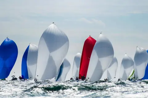 Regata con vele gonfie, bianche, blu e rosse. Le barche della j class solcano le onde agitate in una competizione avvincente.