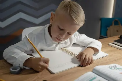 Niño rubio concentrado escribiendo en su cuaderno, practicando el dictado 4 primaria.
