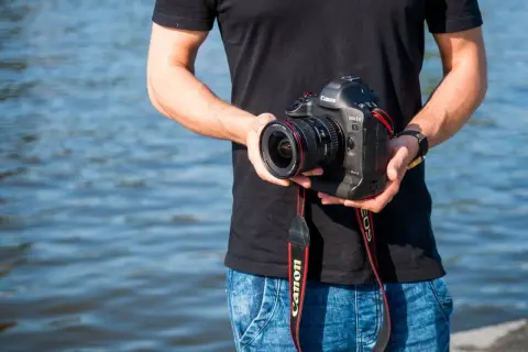 Mężczyzna trzyma aparat Canon EOS-1D Mark II z obiektywem, idealny do fotografii krajobrazowej dzięki matrycy APS-C.
