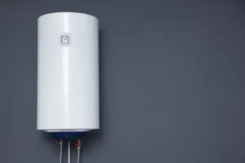 Biały bojler elektryczny wiszący na szarej ścianie.