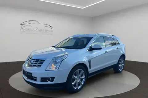 Biały Cadillac SRX z chromowanymi felgami, zaparkowany na obrotowej platformie w salonie samochodowym.