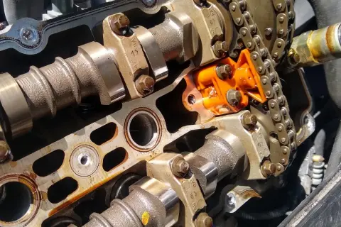 Detalle de un motor con el árbol de levas y el cigüeñal expuestos, junto a una cadena de distribución naranja.