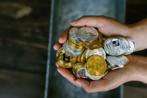Mani che stringono una manciata di monete d'oro e d'argento, simboleggiando i criptovalute rischi e vantaggi.