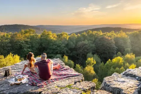 Un couple partage un pique-nique au coucher du soleil sur le roc la tour, surplombant une vallée boisée.