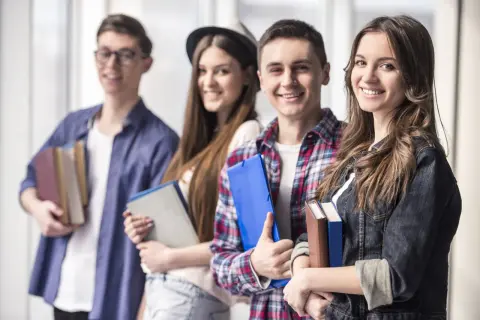 Uśmiechnięci młodzi ludzie z książkami i teczkami. Czy szkoła policealna daje status studenta?
