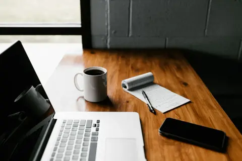 Biurko z laptopem, kubkiem kawy i notatkami. Może to miejsce pracy nad programem Płatnik.