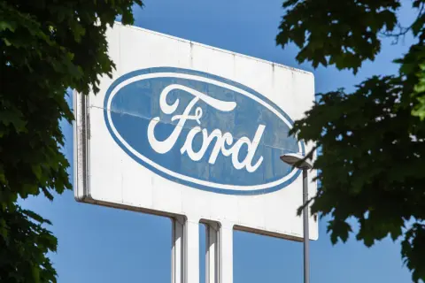 Großes Ford-Logo auf einem Schild, umgeben von grünen Blättern. Vielleicht ein Zeichen für eine neue Ära oder eine ford abfindung.