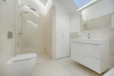 Baño moderno con ducha, inodoro y mueble de lavabo flotante. La decoración de baños pequeños se inspira en la luz y los tonos neutros.