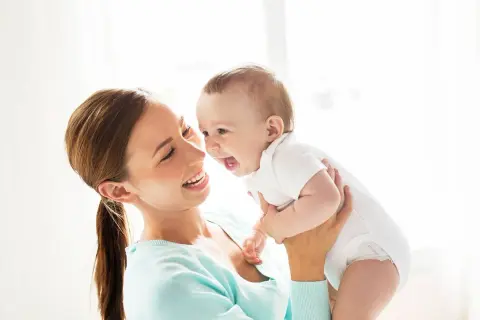 Szczęśliwa mama trzyma roześmiane dziecko. Zastanawiasz się, ile pieluch dziennie dla noworodka?