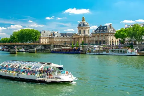 Bateau touristique sur la Seine, avec l'Institut de France et un pont en arrière-plan. Une belle journée pour une visite Paris Seine.