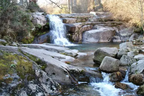 Cascada y charcas naturales en Ourense, rodeadas de rocas cubiertas de musgo y vegetación.