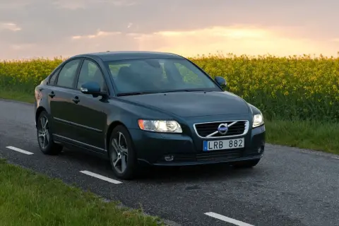 Ciemnozielone Volvo S40 2.0 diesel jedzie wiejską drogą pośród kwitnącego rzepaku.