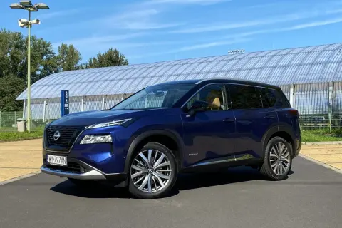 Niebieski Nissan X-Trail na tle hali sportowej. Wiele osób szuka nissan x trail opinie, ten SUV może być dobrym wyborem.