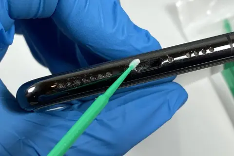 Rękawiczka z niebieskiej gumy delikatnie czyści telefon z kurzu za pomocą zielonego patyczka.