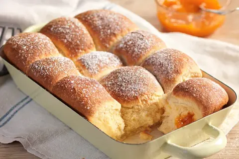 Frisch gebackene Buchteln, bestäubt mit Puderzucker, warten darauf, mit Marillenmarmelade gefüllt zu werden. Ein echtes Buchteln original Rezept.