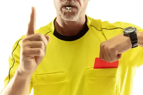 Sędzia z gwizdkiem i czerwoną kartką w ręku, sprawdzający zegarek. Zastanawiasz się, ile zarabia sędzia w Ekstraklasie?