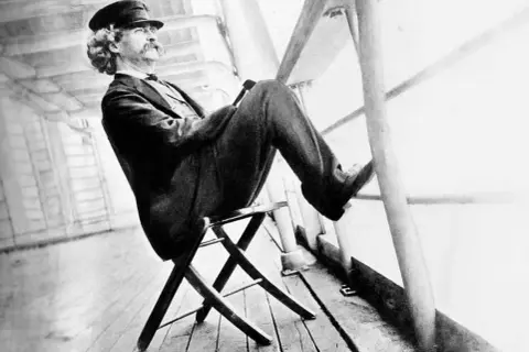 Mark Twain sitter på en stol på ett skeppsdäck, med en hatt och en mustasch. En bild som inspirerar till ett mark twain citat om livet.