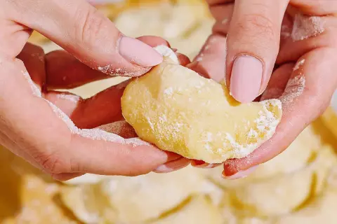 Dłonie z pudrowym cukrem delikatnie formują pyszne pierogi z serem.