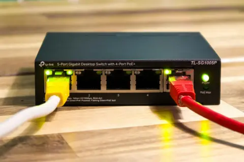 Zarządzalny switch TP-Link TL-SG1005P z 5 portami Gigabit Ethernet i 4 portami PoE+. Podłączone kable sieciowe, świecące diody LED.