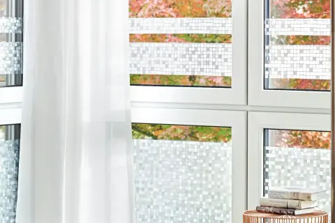 Fenster mit statischer Fensterfolie im Mosaikmuster, die Privatsphäre schafft. Ein weißer Vorhang hängt daneben.