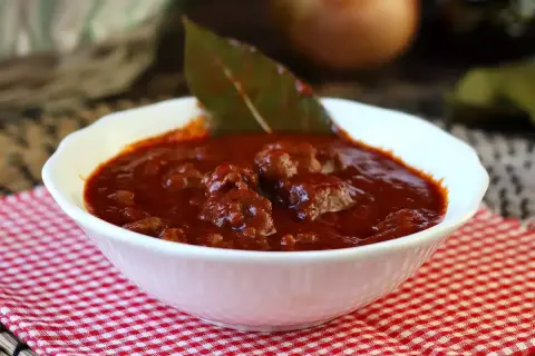 En mustig sås till korv, med köttbitar och lagerblad i en djup röd sås. Perfekt för en mysig middag.