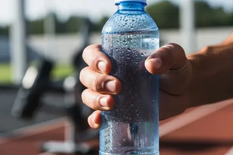 Main d'un sportif tenant une bouteille d'eau fraîche, idéale pour boire de l'eau avec du sel après l'effort.