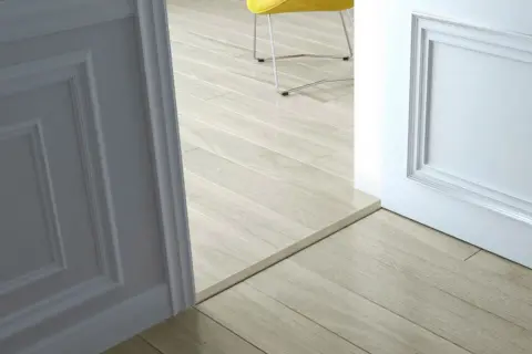 Une alternative barre de seuil discrète sépare deux pièces aux sols en parquet clair.
