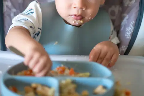 Ett barn med haklapp utforskar sin blw mat på en tallrik.