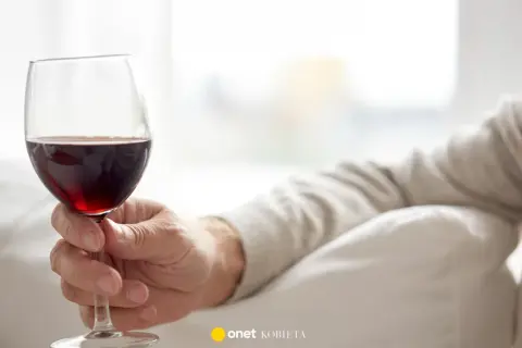 Dłoń trzyma kieliszek czerwonego wina. Czy czerwone wino obniża ciśnienie? Warto to sprawdzić.