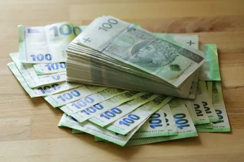 Stos banknotów 100 zł i 100 euro na drewnianym blacie. Może to być kwota na zasiłek stały.