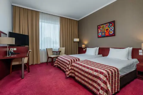 Pokój w hotelu Premier Kraków z dwoma wygodnymi łóżkami, biurkiem i kolorowym obrazem na ścianie.