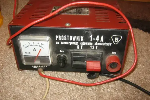 Stary prostownik pokazuje zero, kiedy akumulator jest naładowany. Czerwony kabel wisi swobodnie.